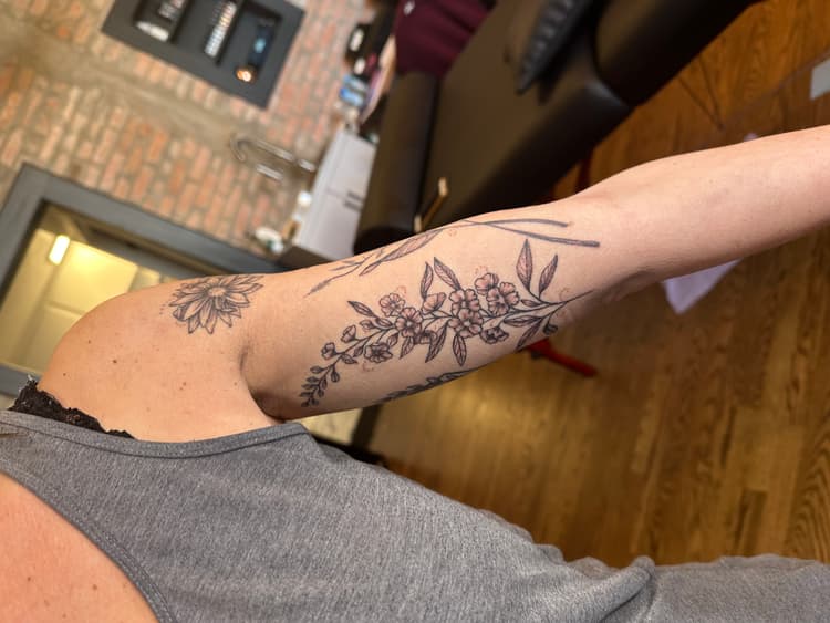 Black botanical floral tattoo on a person's arm with leaves and flowing design