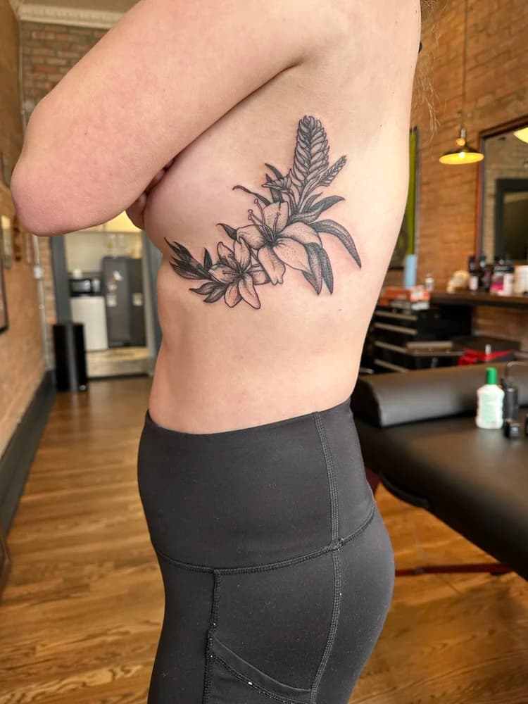 Black ink floral tattoo on side ribcage featuring daisies and leaves with text