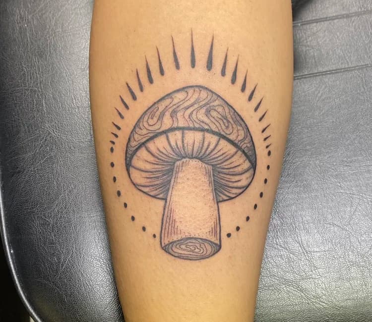 Black ink mushroom tattoo on shin with radiating lines and dot work details