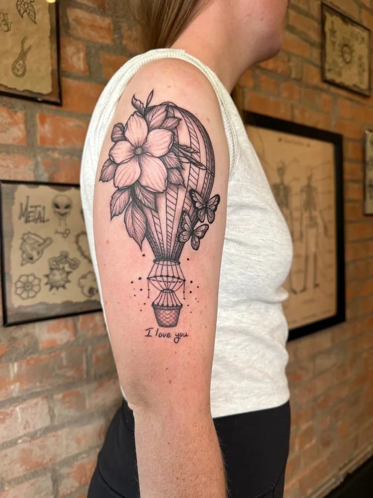 Black ink hot air balloon tattoo on arm with floral basket and text quote