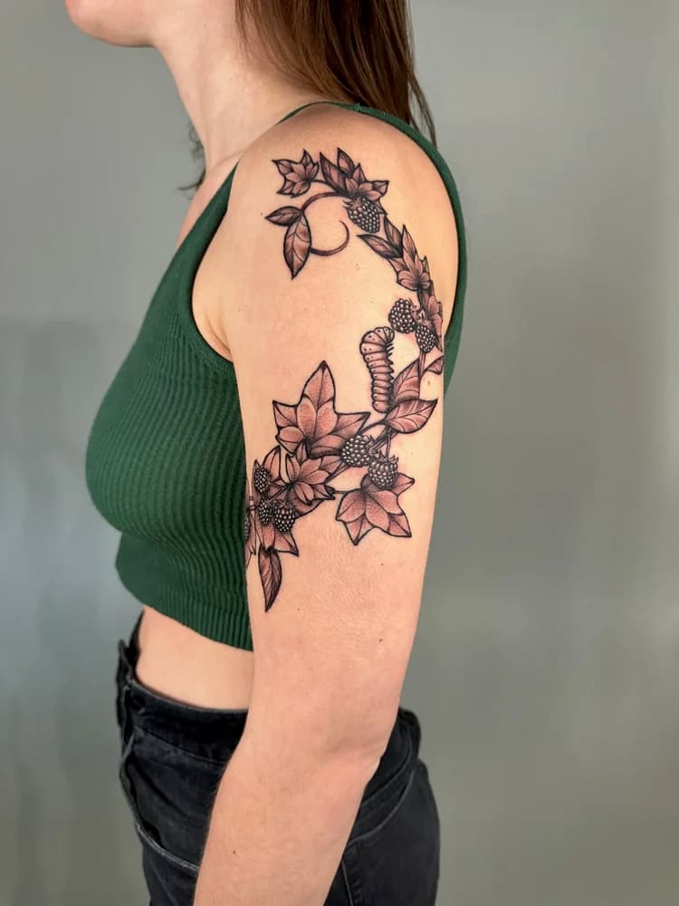 Black ink shoulder tattoo with flower and berry floral design on upper arm