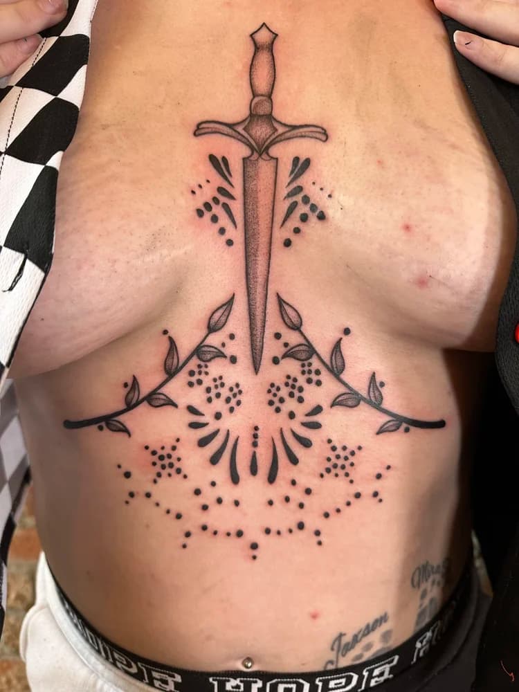 Black and gray ornamental sword tattoo on chest with symmetrical decorative elements