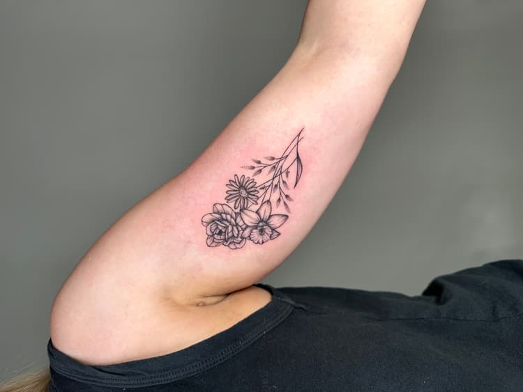 Black botanical flower buds tattoo on inner arm with delicate line work