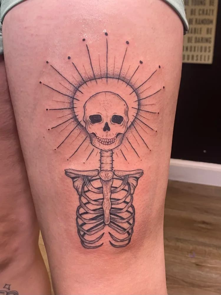 Black and gray skull and ribcage tattoo on thigh with radiating line details