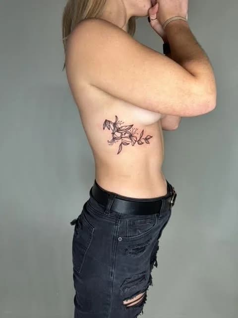 Black botanical small tattoo on ribcage featuring flowers and decorative line art